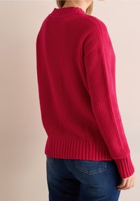 Fuksiavärinen neulepaita, jossa on ribbaus kauluksessa, pitkissä hihoissa ja ribattu helma. Yhdistettynä sinisiin farkkuihin, näyttää tekstuuripintaa takanäkymästä.