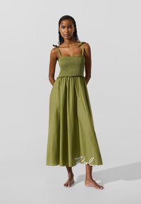 Roheline maksikleit, millel on kortsuline korsettosa, õhukesed rihmad paeltega ning voolav, sile tekstuur, mis ulatub kuni pahkluudeni.