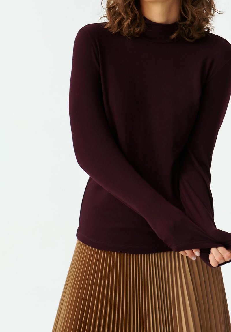 Burgundy pitkähihaineen turtleneck-paita, joka on valmistettu pehmeästä kankaasta, yhdistettynä laskostettuun vaaleanruskeaan hameeseen, joka tarjoaa sileän pinnan ja muotoillun designin.