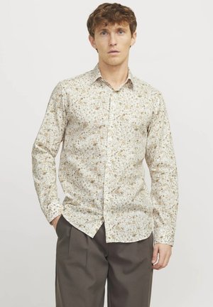 Chemise à imprimé floral en crème clair, ornée de petites fleurs brunes et vertes. Manches longues, col boutonné, coupe décontractée, avec une texture lisse.