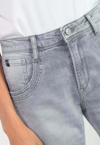 Jean en denim gris clair avec une coupe classique. Comprend une poche avant, une fermeture à bouton et un léger décoloré pour une variation de texture.