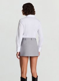 White long-sleeve shirt with a collar, paired with a short, gray skirt. The skirt features a fitted waistband and smooth texture.
