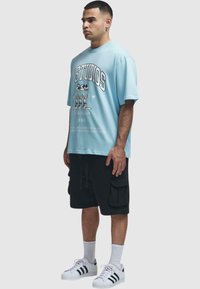 Světle modré oversized tričko s grafickým potiskem, doplněné černými cargo šortkami. Stylizováno s bílými ponožkami a černobílými teniskami.