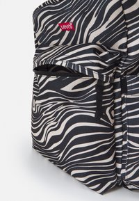 Svart-och-vitt randig tyg ryggsäck med en röd Levi's-logo, som har dragkedjefickor, justerbara remmar och en slät textur.