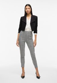 Černá zkrácená bunda přes bílou blůzu; doplněno o přiléhavé kostičkované kalhoty v černobílé barvě; modelka má na sobě černé špičaté lodičky.