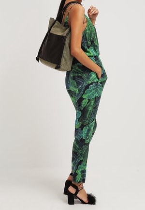 Jumpsuit con stampa a foglie verdi, dalla vestibilità morbida e dotato di tasche, abbinato a uno zaino bicolore nero e oliva e sandali platform neri.