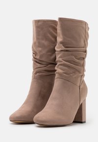 Taupe high-heel ankle boots in soft suede, featuring a slouchy design with gathered material and a block heel for stability.