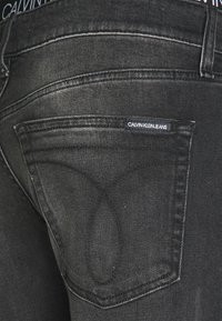 Černé džíny z denimu s páskem Calvin Klein, jemným vyblednutím, zadní kapsou s logem a dekorativním prošíváním na kapse.