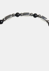Bracciale nero e argento con perline nere rotonde, accenti cilindrici metallici e piccole sfere lucide, con una texture liscia.