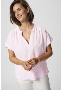 Blouse en lin rose clair avec un col en V et des manches courtes, présentant de douces fronces aux épaules et une coupe décontractée.