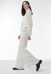 Witte gebreide coltrui en bijpassende wijde broek, beide met een zachte textuur. Zwarte enkelboots met een chunky hak passen goed bij de outfit.