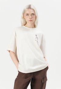 Beige short-sleeve t-shirt with a crew neckline, featuring a graphic design of a sun and wave. Fabric appears soft with a relaxed fit.