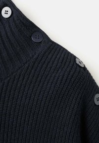 Granatowy sweter dzianinowy o prążkowanej fakturze, z trzema dużymi czarnymi guzikami wzdłuż szwu na ramieniu dla dodatkowego efektu.