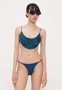 Teal bikini med en rynket topp med justerbare stropper og matchende lavtkuttede underdeler. Glatt tekstur og minimalistisk design.