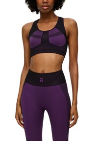 Lila und schwarze athletische Cropped-Top mit einem gemusterten Design und einem Logo auf der Vorderseite. Kombiniert mit hoch taillierten lila Leggings.