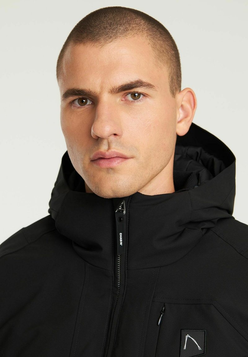 Czarna kurtka z kapturem, z zamkiem z przodu, teksturowanym materiałem i małym logo w górnej lewej części klatki piersiowej.