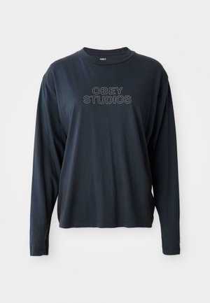 Fekete, hosszú ujjú pamut póló, kerek nyakkivágással és elől egy grafika, amely "OBEY STUDIOS" felirattal szerepel, kontrasztos fehér betűkkel.