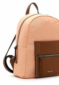 Sac à dos en nylon rose avec des accents en cuir marron, doté d'une poche zippée à l'avant et de deux bretelles réglables. Texture lisse et forme arrondie.