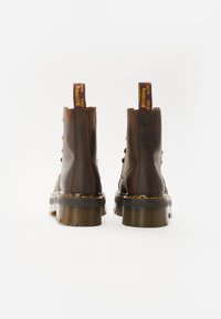 Bottines en cuir marron avec une finition texturée, semelles transparentes épaisses et une languette de marque jaune à l'arrière. Six œillets pour le laçage.