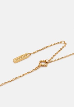 Chaîne en or avec une petite plaque rectangulaire gravée "BURTON" et un fermoir anneau ressort sur fond blanc.