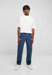T-shirt blanc surdimensionné, pantalon bleu à jambe droite et baskets blanches. Tissu lisse, coupe décontractée et design casual. Couleurs simples et unies.