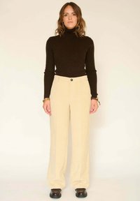 Pull en laine brun à col roulé côtelé associé à un pantalon en velours côtelé beige à jambes larges. Le pantalon présente une fermeture à bouton à l'avant et un subtil design à rayures verticales.