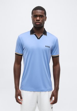 Ung mand iført en lyseblå polo med sort og beige krave og ærmekant samt hvide shorts med "BOSS"-logo.