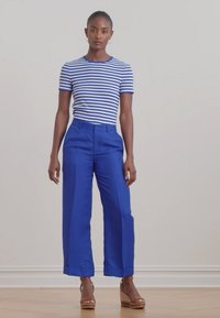 Chemise à rayures à manches courtes en bleu et blanc, associée à un pantalon large bleu vif. Des chaussures à talons en bois ajoutent de la hauteur et un contraste.