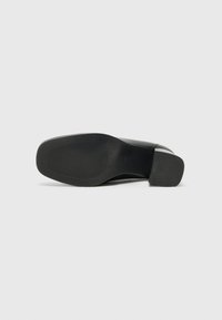 Scarpa nera con tacco alto, finitura liscia, punta rotonda e suola in gomma testurizzata con linee orizzontali per una migliore aderenza.