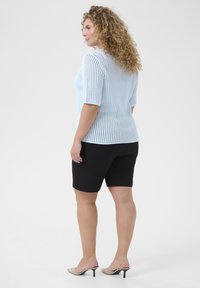 Un haut tricoté bleu clair à manches courtes avec un motif texturé associé à un short noir. Des chaussures à talons beiges complètent la tenue.