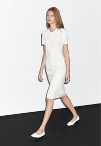Biała dopasowana koszulka z krótkim rękawem, połączona z białą ołówkową spódnicą wykonaną z gładkiego materiału oraz białymi butami typu slip-on. Minimalistyczny design.