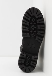 Schwarze robuste Stiefelsohle mit tiefen Profilen und rautenförmigen Griffen. Auf der Seite befindet sich das Markenlabel "TOMMY JEANS" und die Größe "37".