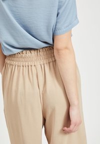 Jasnoniebieska koszula z krótkim rękawem w luźnym fasonie, w połączeniu z beżowymi, luźno dopasowanymi spodniami z marszczoną elastyczną talią.