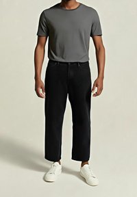 Šedé tričko s krátkým rukávem, kombinované s černými džíny s rovnými nohavicemi a bílými teniskami, s jednoduchým designem bez vzorů nebo zdobení.