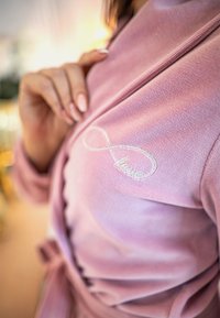 Accappatoio in pile rosa con cintura in satin, decorato con un simbolo dell'infinito ricamato in argento e la parola "amore" sul petto.