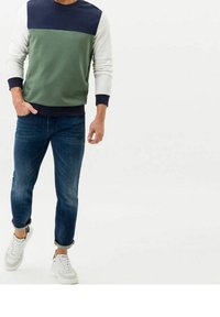 Men's sweatshirt in green, navy, and white color-block design. Soft fabric, crew neck, ribbed cuffs and hem. Paired with blue jeans and white sneakers.