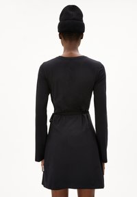 Svart långärmad klänning i mjukt tyg, med bälte vid midjan och knälång nederkant, samt rund halsringning.
