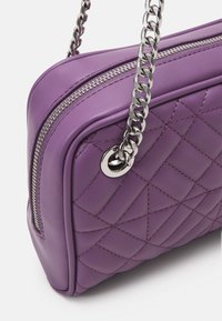 Borsa a tracolla in pelle viola con motivo trapuntato, catena in tonalità argento e chiusura con zip. Presenta bordi arrotondati e dettagli di cucitura sottili.