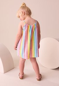 Gestreepte peuterjurk met dunne bandjes, met verticale regenboogstrepen in pasteltinten. Zachte stof met een geplooide achterkant.