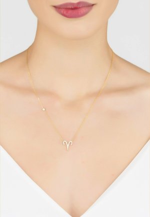 Gold chain necklace featuring a sparkly Aries symbol pendant with a smaller round accent, displayed against a bare neckline.