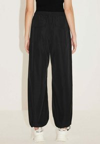 Zwarte high-waisted wijde broeken met elastische tailleband, voorzien van zijzakken en taps toelopende manchetten, gecombineerd met witte sneakers.