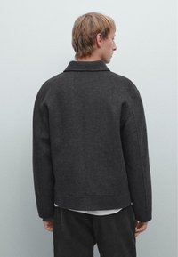 Dark gray wool blend jacket with a classic collar, relaxed fit, and ribbed hem. Features seamless shoulder design and mid-length sleeves.