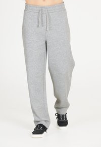 Grå sweatpants lavet af blødt stof, med elastisk talje og snøre, afslappet pasform og sidelommer. Sorte sneakers synlige.