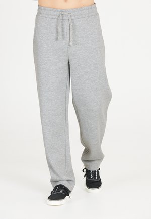 Grijze sweatpants van zacht materiaal, met een elastische tailleband met een trekkoord, een relaxte pasvorm en zijzakken. Zwarte sneakers zichtbaar.