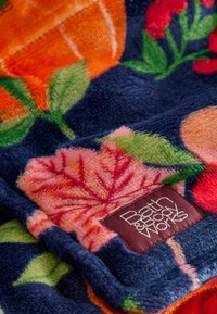 Pătură din fleece cu un fundal albastru marin, având modele florale colorate în portocaliu, roz și verde; include o etichetă de la Bath & Body Works.
