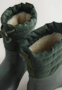 Bottes en caoutchouc vertes avec doublure en peluche beige, dotées d'un haut pliable, d'une fermeture à cordon et d'une surface texturée pour une meilleure adhérence.