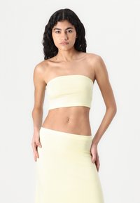 Yellow strapless top made of soft fabric, featuring a snug fit. The model pairs it with a matching pastel yellow skirt.