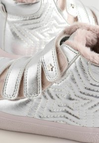 Sneaker metallic argentati con motivo a stelle testurizzato, interno in pelliccia sintetica rosa e cinturini regolabili in Velcro. Suola in gomma per una buona aderenza.