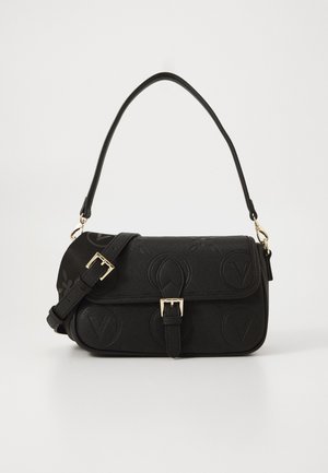Sac à épaule noir avec motifs circulaires embossés, sangle réglable, fermeture à boucle dorée et une seule poignée supérieure sur fond uni.