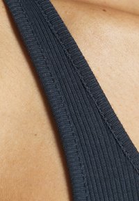 Tessuto ribbed grigio scuro di un top senza maniche, che mostra una superficie texture e spalline larghe su uno sfondo di pelle chiara.